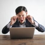 Man with glasses looking suprised at his laptop
