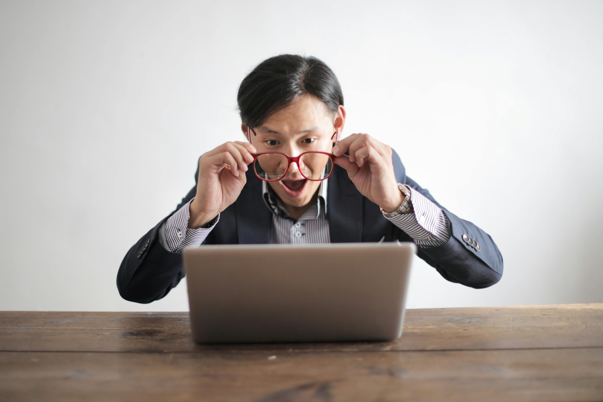 Man with glasses looking suprised at his laptop